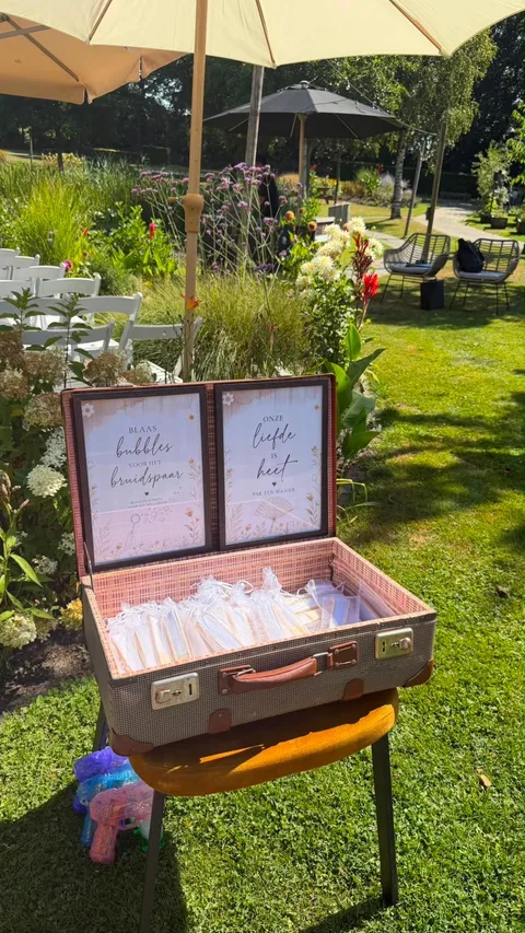 Vintage koffer met bordjes ‘blaas bubbles’ en ‘pak een waaier’ in een trouwtuin
