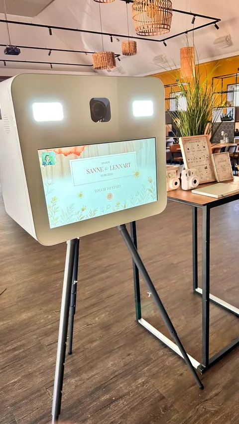 De witte photobooth van Studio SOVA op statief in een feestzaal, met welkomstscherm